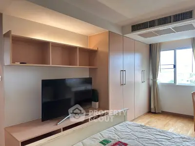 Spacious bedroom with built-in wardrobe and modern TV setup, featuring natural light from large window.