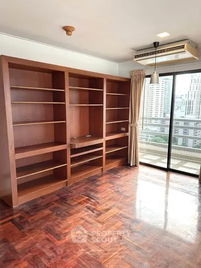 Spacious study room with built-in wooden shelves and city view balcony.