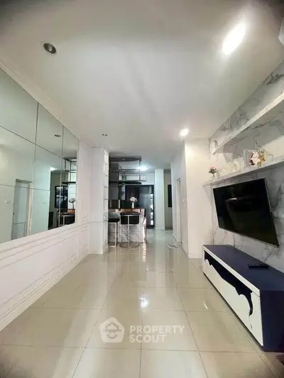 Spacious modern living room with sleek design and wall-mounted TV, leading to a stylish kitchen area.
