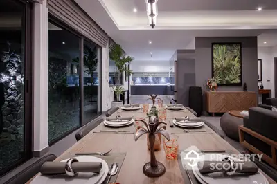 Elegant dining area seamlessly connects to a cozy living space, featuring a long wooden table set for a sophisticated gathering, with modern lighting and large sliding glass doors offering a view of the tranquil outdoor area.