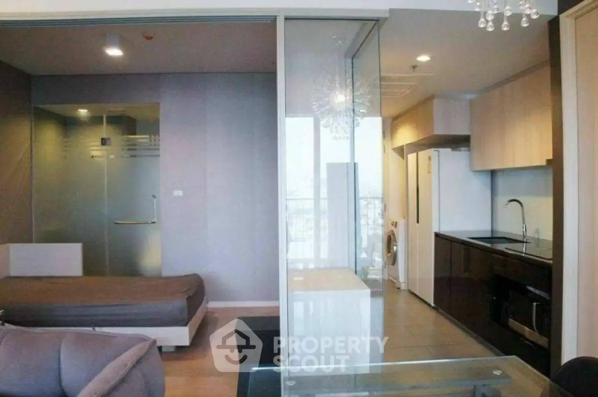 Modern studio apartment with glass partition, sleek kitchen, and cozy living area.