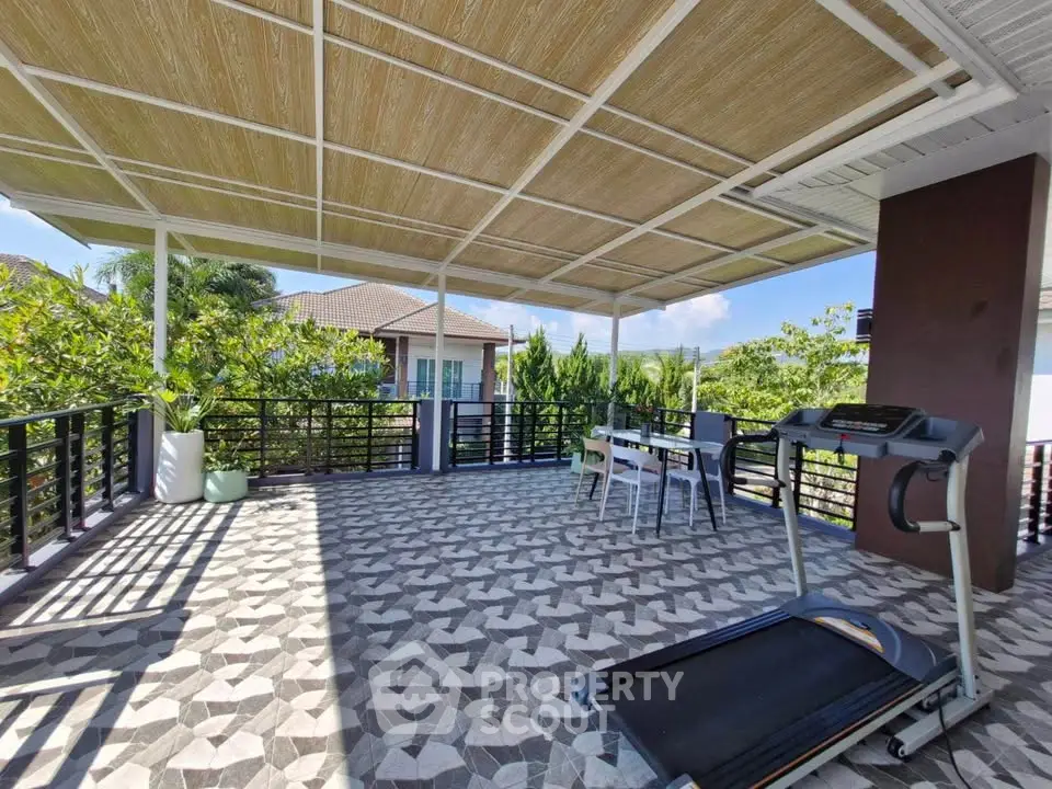 Spacious rooftop terrace with treadmill and outdoor dining set, surrounded by lush greenery.