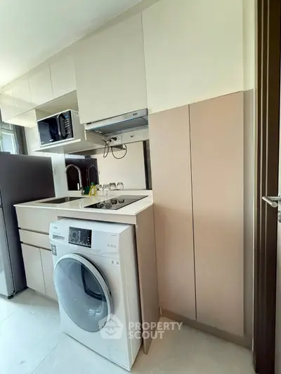 Modern kitchen with sleek appliances and compact design, featuring a washing machine and microwave.