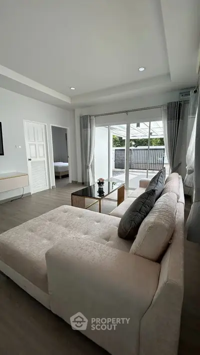 Spacious living room with modern decor and large windows opening to a balcony.