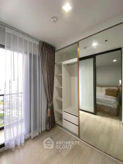 Modern bedroom with mirrored wardrobe and large window offering natural light.