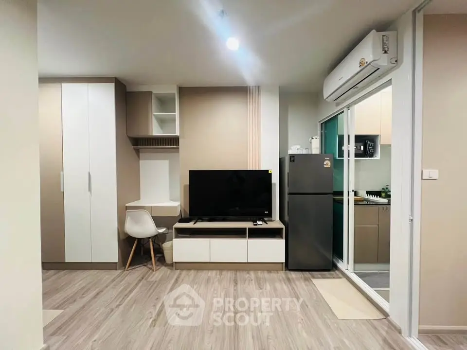 Modern living room with sleek furniture and open kitchen layout, featuring a TV and air conditioning.