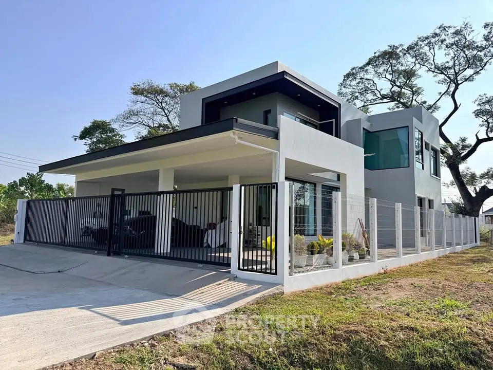 Modern two-story house with sleek design and spacious driveway, surrounded by a stylish fence and lush greenery.