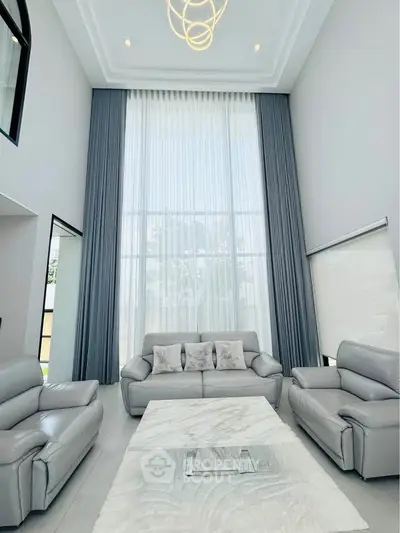 Luxurious high-ceiling living room with elegant gray sofas and large windows.