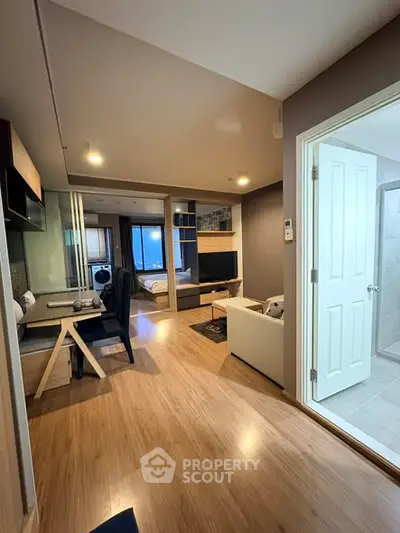 Modern studio apartment with open layout and wooden flooring, featuring a cozy living area and a glimpse of the bathroom.