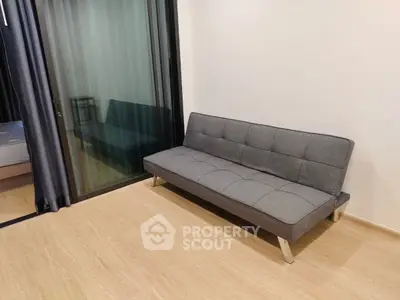 Modern apartment with sleek sofa and glass sliding doors leading to bedroom.