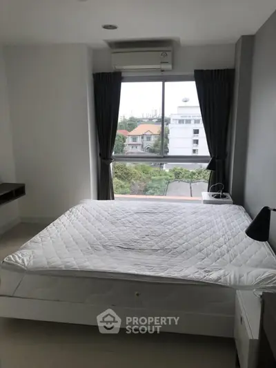 Modern bedroom with large window and city view, featuring a comfortable bed and sleek design.