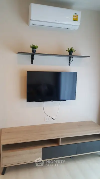 Modern living room with wall-mounted TV and air conditioner, sleek wooden console, and decorative plants.