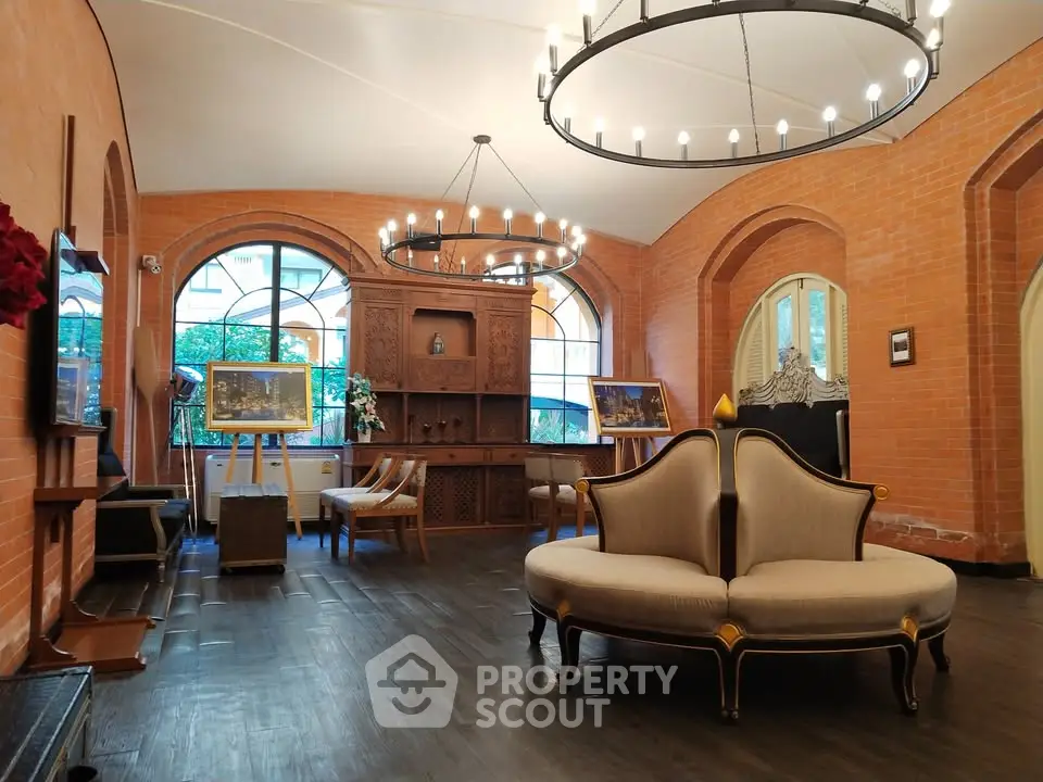Elegant living room with vintage furniture and brick walls, featuring large windows and chandeliers.