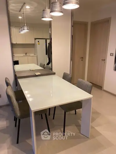 Modern dining area with sleek table and chairs, adjacent to a minimalist kitchen with contemporary lighting.
