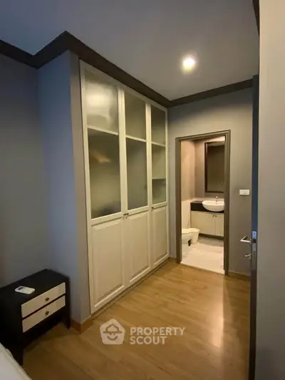 Modern bedroom with wooden flooring and built-in wardrobe leading to a sleek ensuite bathroom.