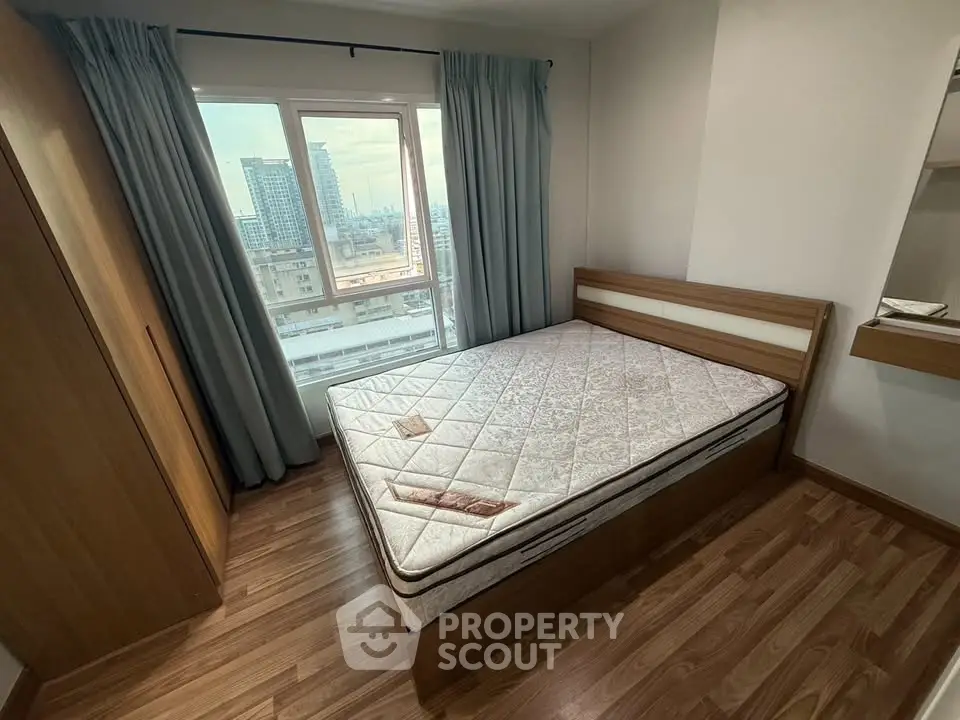 Cozy bedroom with wooden flooring and large window offering city views, featuring a comfortable bed and wardrobe.