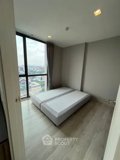 Modern bedroom with large window offering city views, featuring minimalist design and ample natural light.