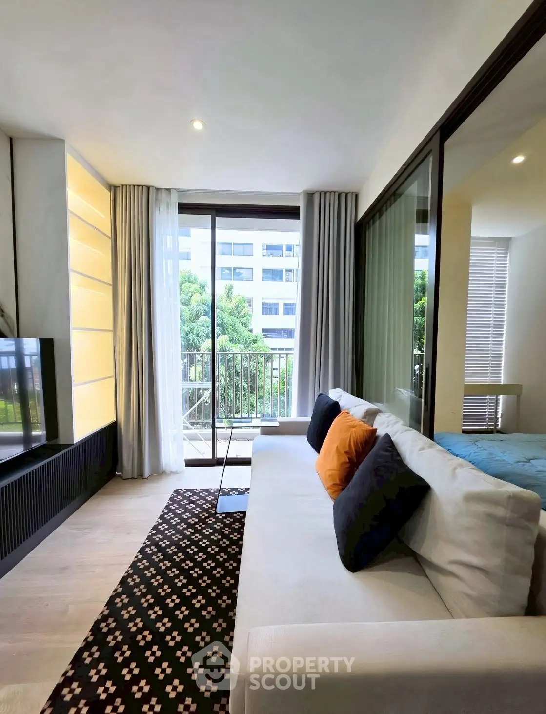 Modern living room with cozy sofa and large windows offering a view of lush greenery and urban landscape.