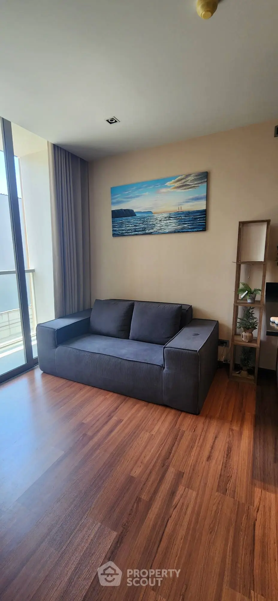 Modern living room with sleek gray sofa and wooden flooring, featuring a large window with natural light.