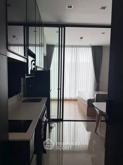 Modern studio apartment with sleek kitchen and cozy bedroom separated by glass partition.