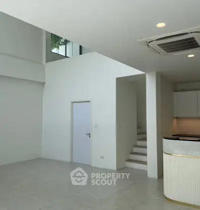Spacious modern interior with high ceilings and sleek design, featuring a staircase and open kitchen area.
