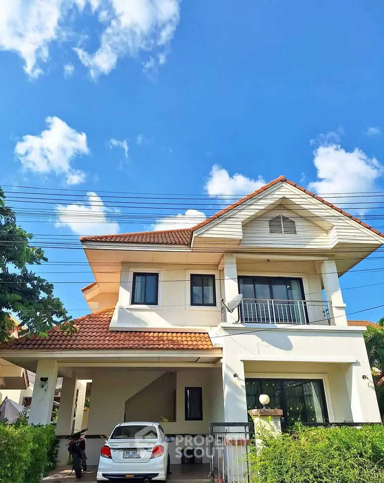 Charming two-story house with red-tiled roof and carport under a clear blue sky.