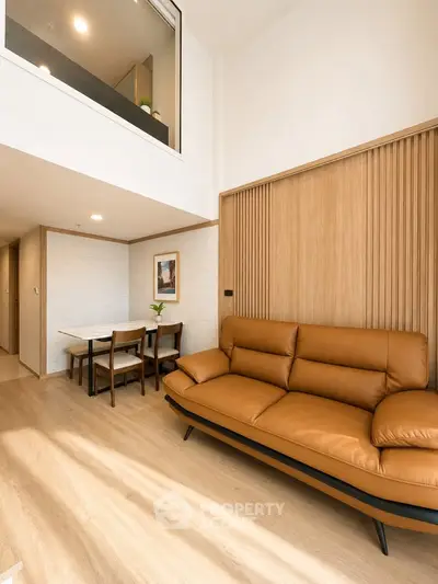 Modern living room with stylish leather sofa and dining area in open-plan apartment.