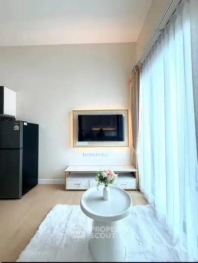 Bright living room with modern decor and large window, featuring a wall-mounted TV and cozy seating area.