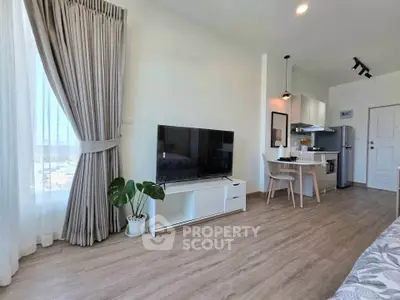 Modern open-plan living room with kitchen, featuring sleek furniture and large window for natural light.