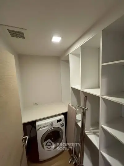 Spacious laundry room with modern washing machine and ample shelving for storage.