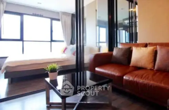 Modern living room with leather sofa and glass partition leading to a cozy bedroom.