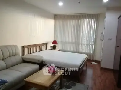 Cozy bedroom with wooden flooring, comfortable sofa, and natural light from large window.