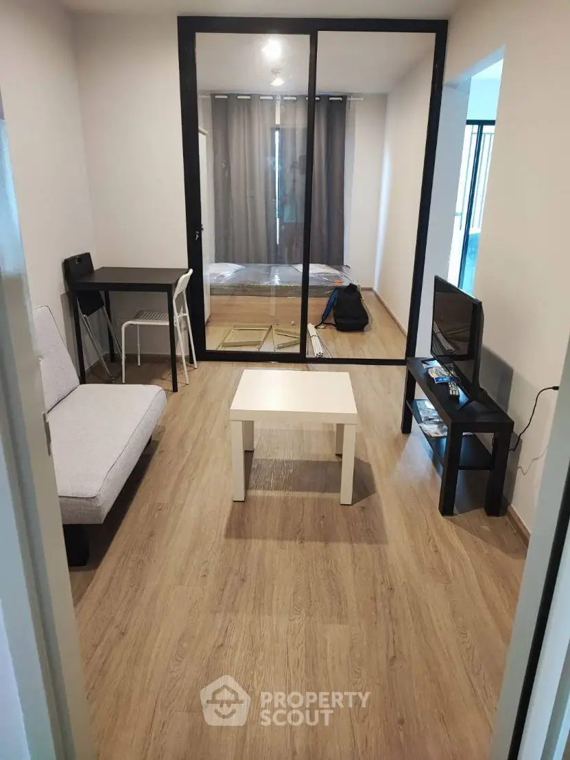 Modern living room with sleek furniture and glass partition leading to bedroom.