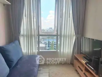 Cozy living room with large window offering stunning city view, featuring a comfortable sofa and modern TV setup.