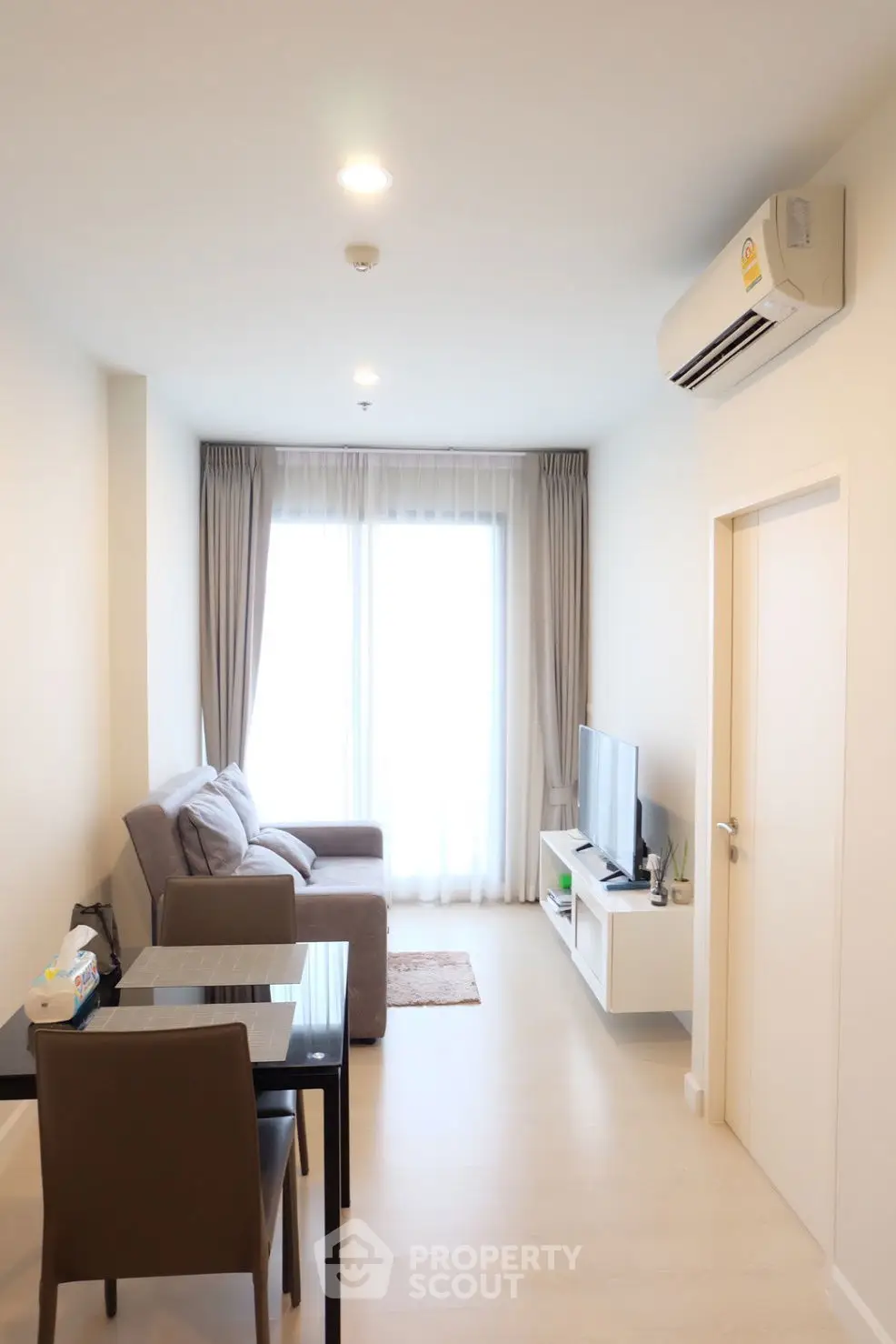 Modern living room with cozy sofa, dining table, and wall-mounted TV in bright apartment.
