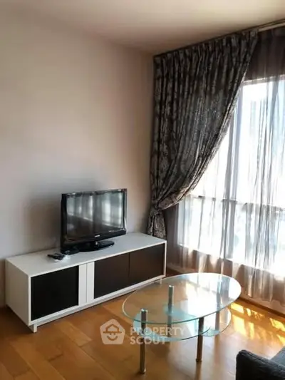 Cozy living room with TV stand, glass coffee table, and elegant curtains.