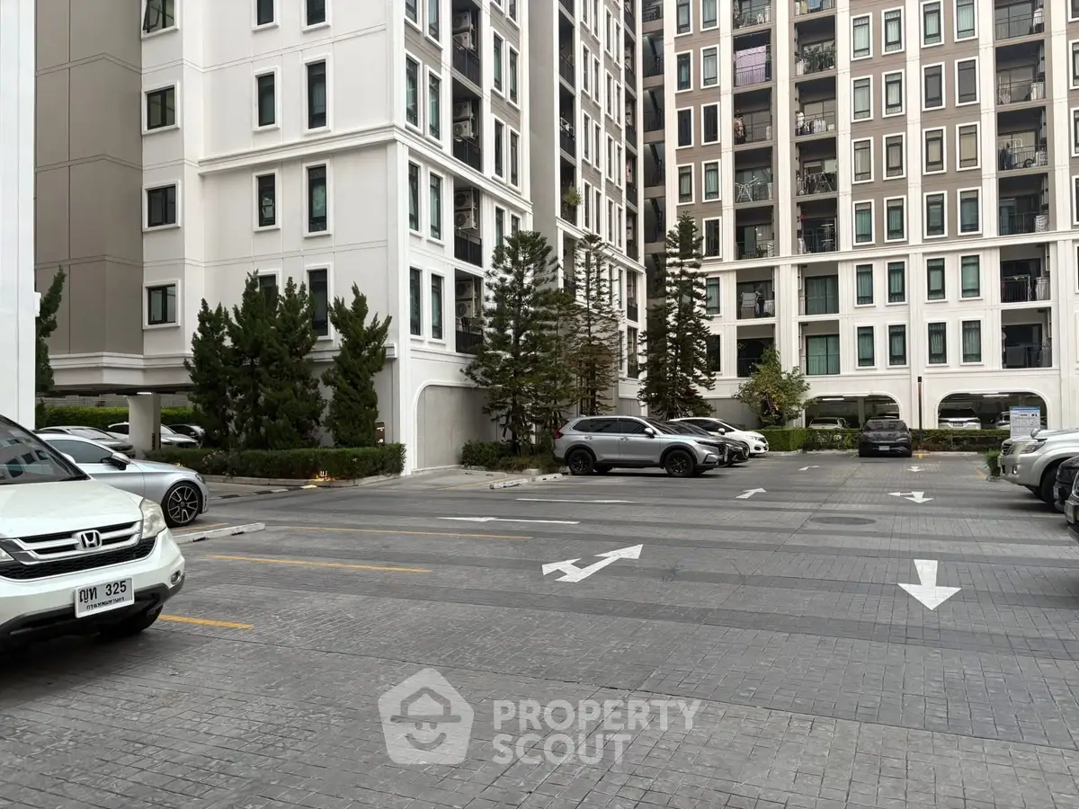 Modern apartment building with spacious parking area and lush greenery.