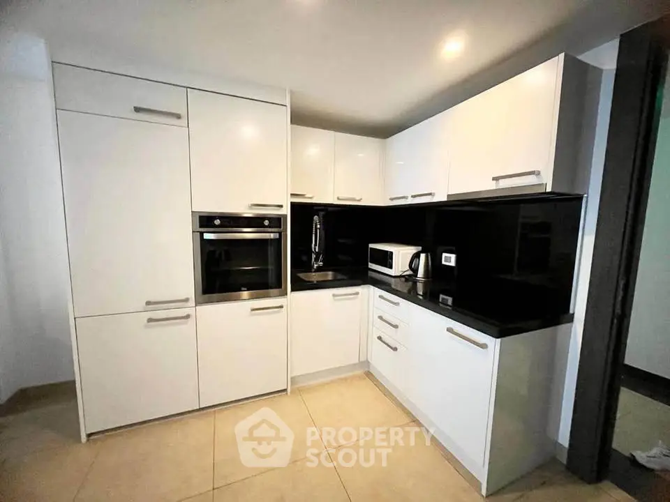 Modern kitchen with sleek white cabinets and built-in oven, featuring a minimalist design and black countertops.
