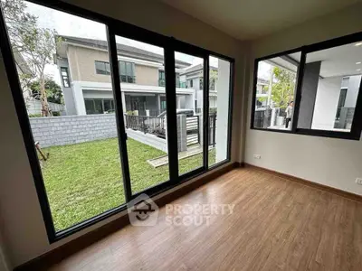 Spacious room with large windows offering a view of a modern house and garden.