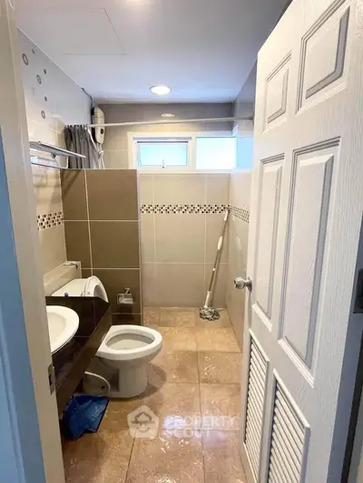 Modern bathroom with tiled walls and floor, featuring a toilet and sink.
