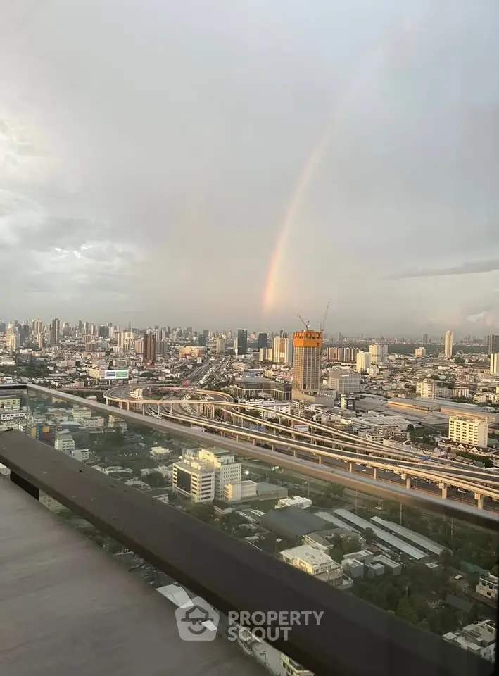 Stunning cityscape view with rainbow from high-rise balcony, perfect urban living experience.