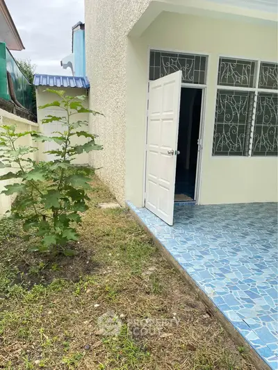 Charming property with tiled patio and garden area, featuring a welcoming entrance and lush greenery.