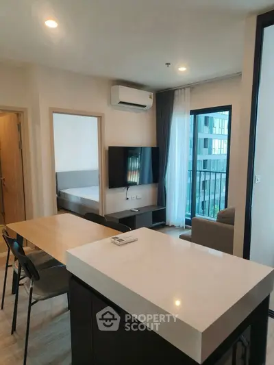 Modern open-plan living area with sleek kitchen and cozy seating, featuring large windows for natural light.