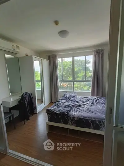 Bright bedroom with large windows and modern furnishings, offering a serene view of lush greenery.