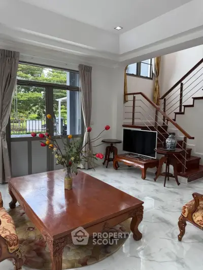 Elegant living room with wooden furniture and staircase, featuring large windows and garden view.