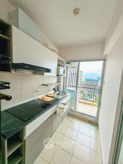 Modern kitchen with open layout and balcony view, featuring sleek appliances and ample natural light.