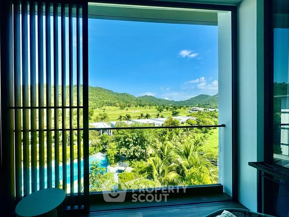 Stunning view from modern apartment window overlooking lush greenery and mountains.