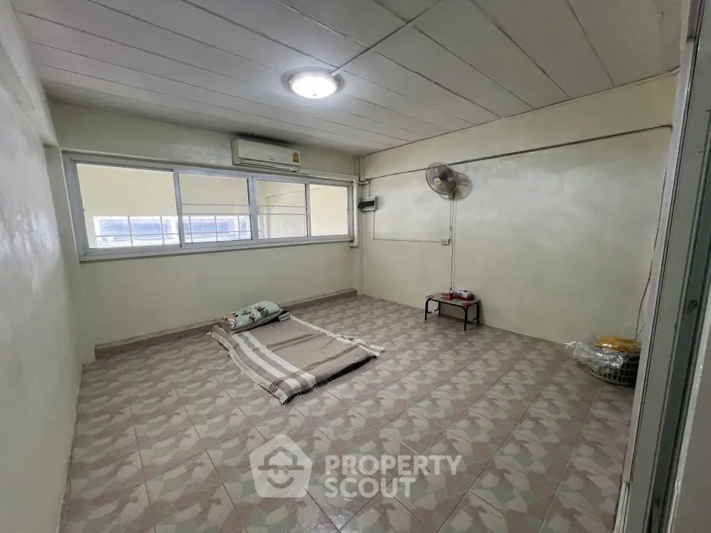 Minimalist bedroom with tiled floor and large window, featuring a simple mattress setup.