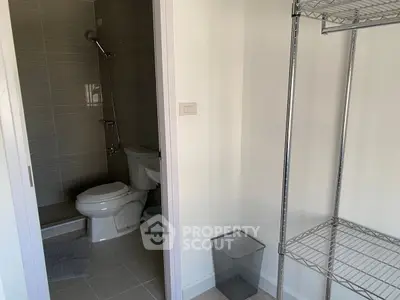 Compact bathroom with modern fixtures and metal shelving unit, ideal for efficient space utilization.