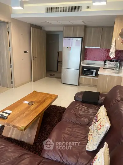 Modern living room with cozy leather sofa, wooden coffee table, and sleek kitchen area with red backsplash.